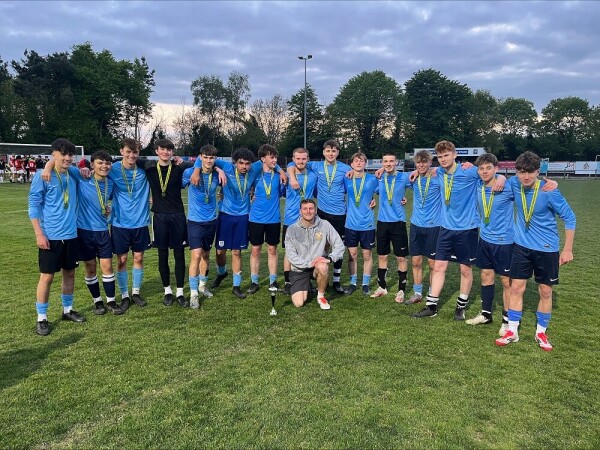 The team standing on the pitch wearing blue shirts and their medals